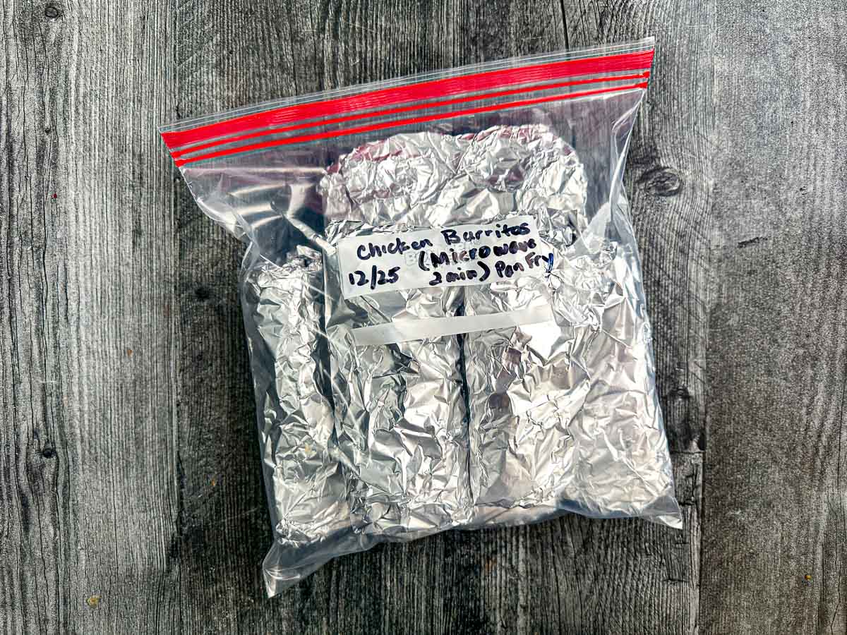 Large ziplock bag with aluminum wrapped frozen meal plan burritos that's labeled with instructions for reheating.