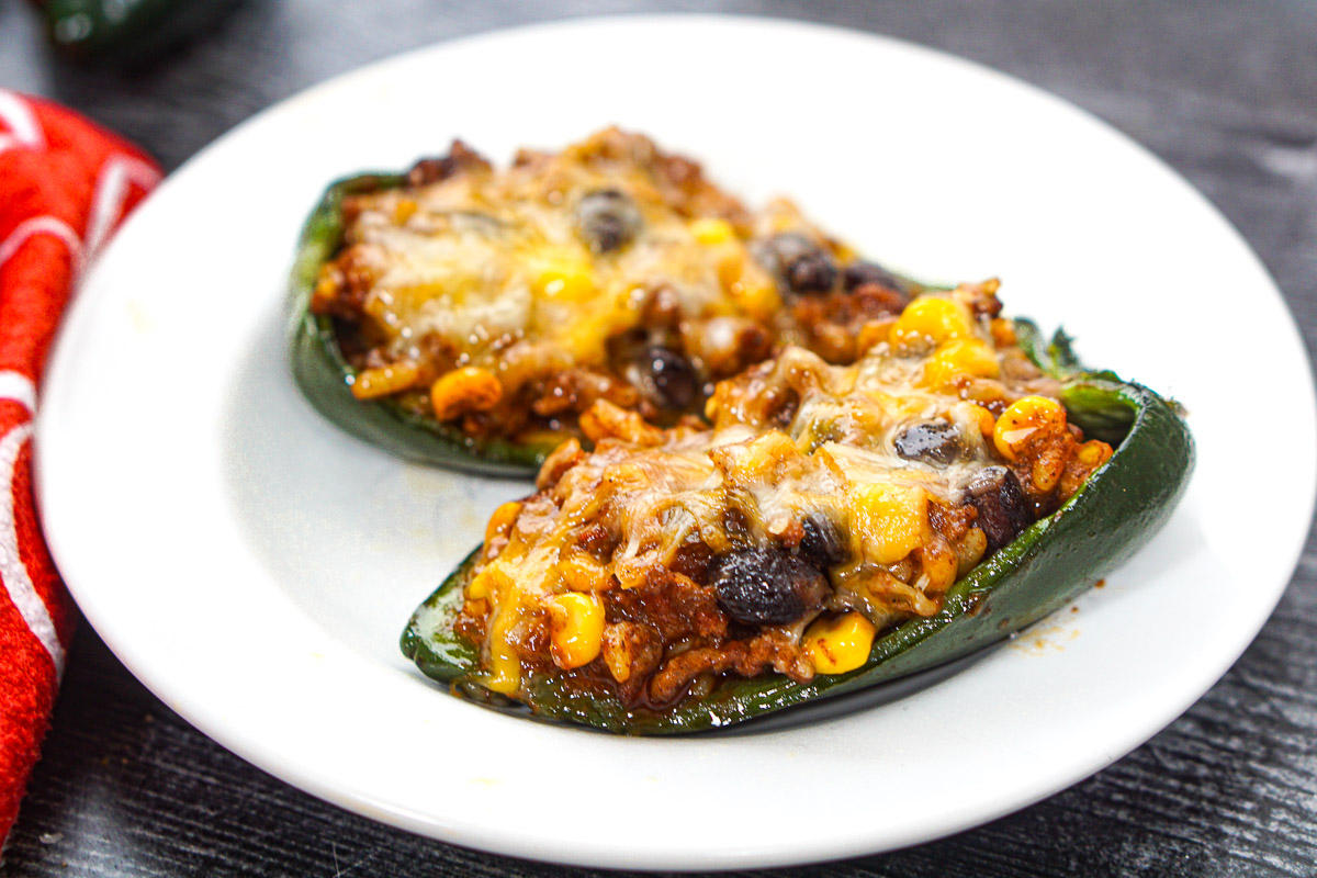 Closeup of a plate with 2 Mexican stuffed poblanos with melted cheese on top.