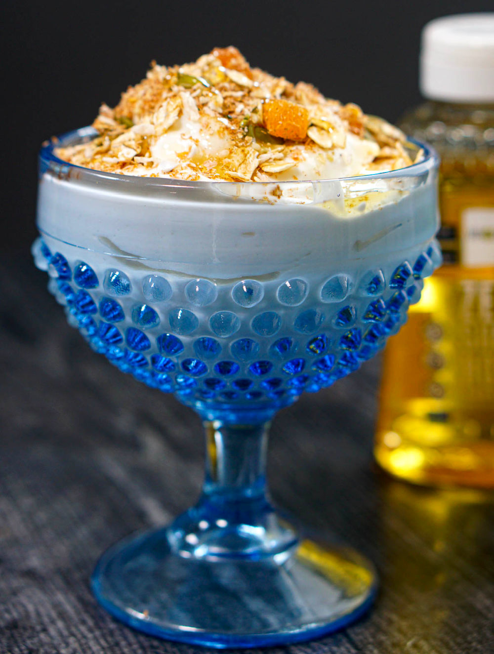 Closeup of a blue glass dessert dish with greek yogurt topped with muesli mix and keto honey.