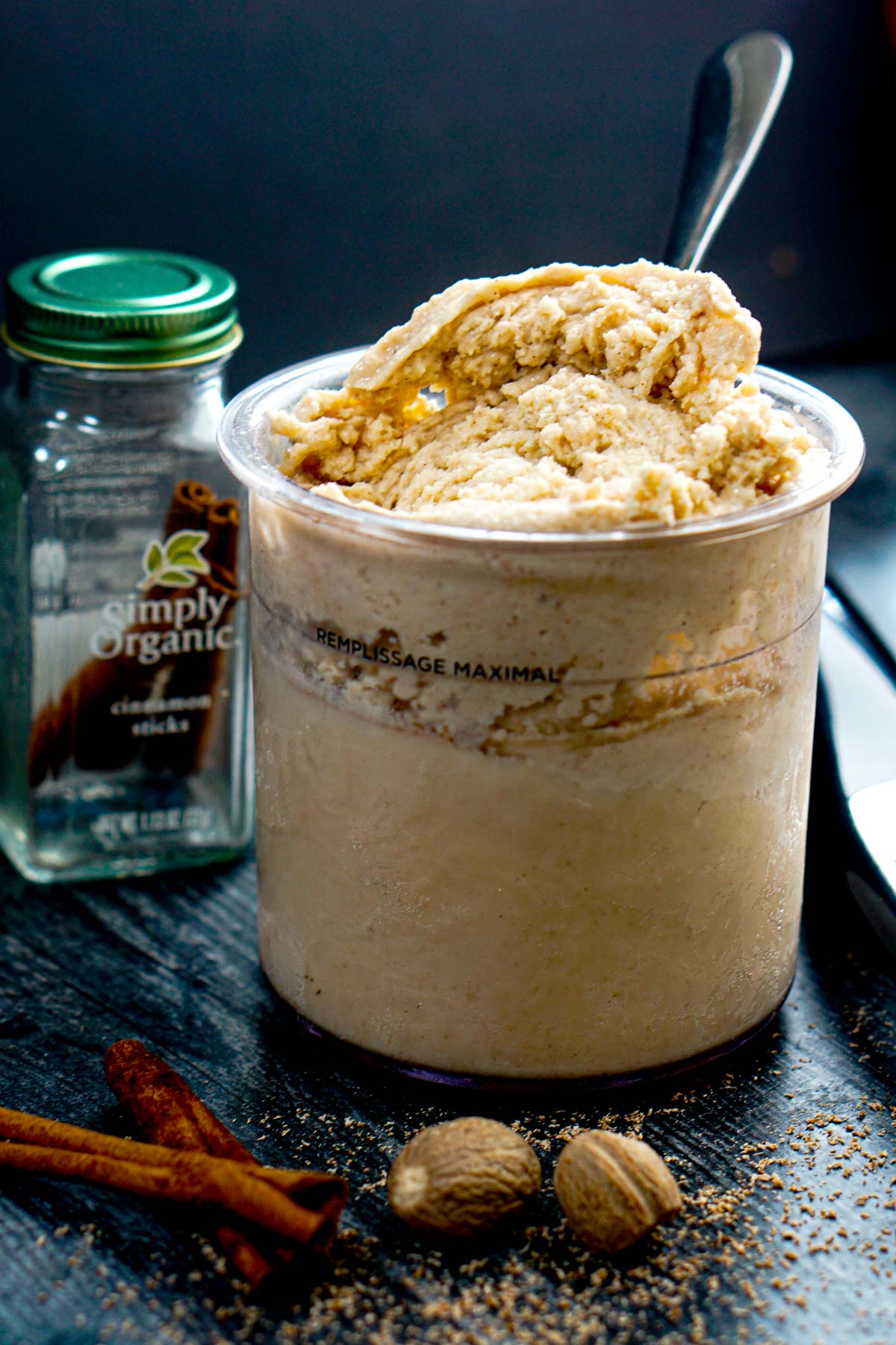 Closeup of a pint of Ninja Creami keto egg nog ice cream that's high protein along with cinnamon sticks and nutmeg.