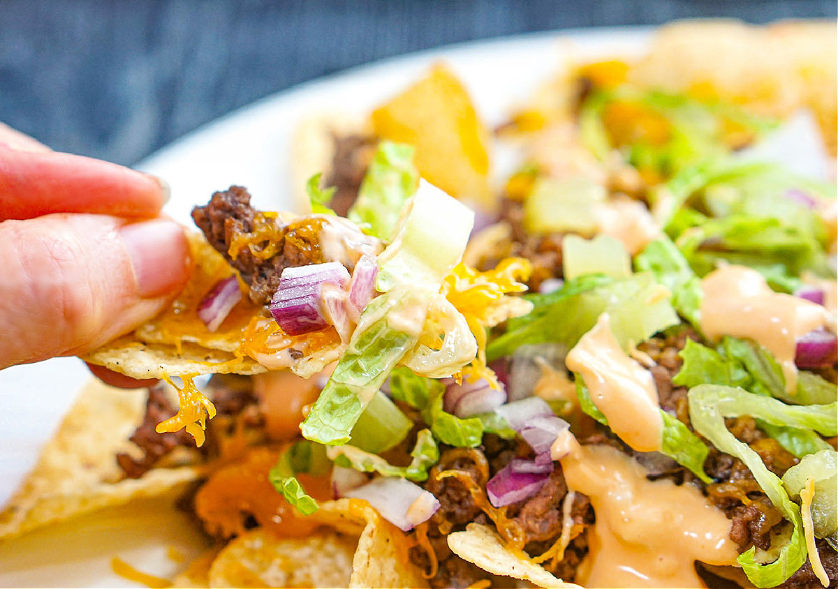 Fingers holding up a chips filled with Big Mac filling.