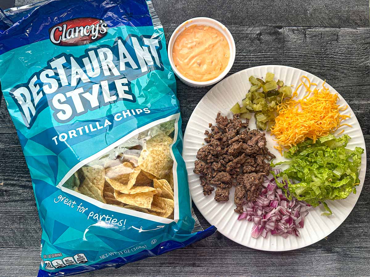 Recipe ingredients - tortilla chips, special sauce, browned ground beef, chopped pickles, cheese, onions and lettuce.