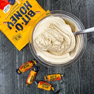 Aerial view of a pint container with keto bit o honey ice cream made in the Ninja Creami and some scattered candies next to i.