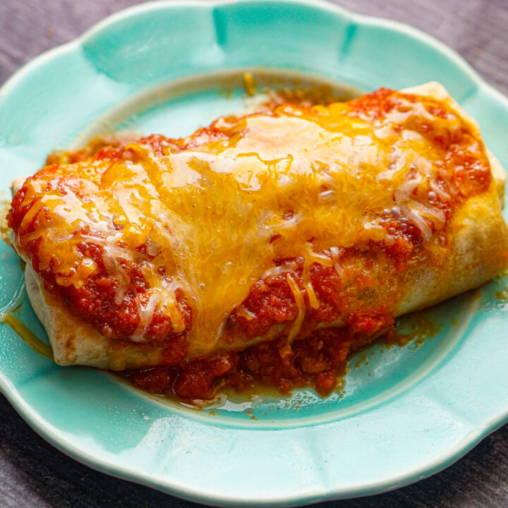 Aqua plate with a cooked chicken burrito with salsa and cheese on top.