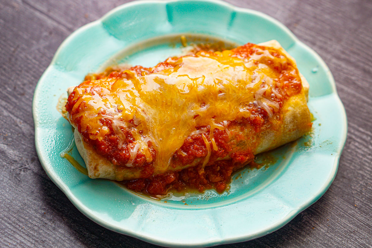 Aqua plate with one of the cooked chicken meal plan burritos with salsa and cheese on top.