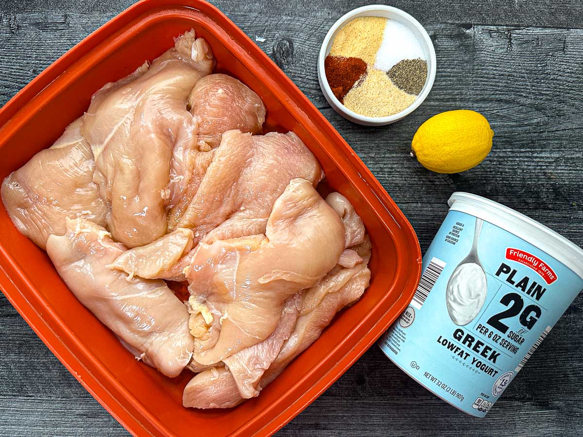 Marinating container with raw chicken and ingredients for marinade - yogurt, lemon and spices.