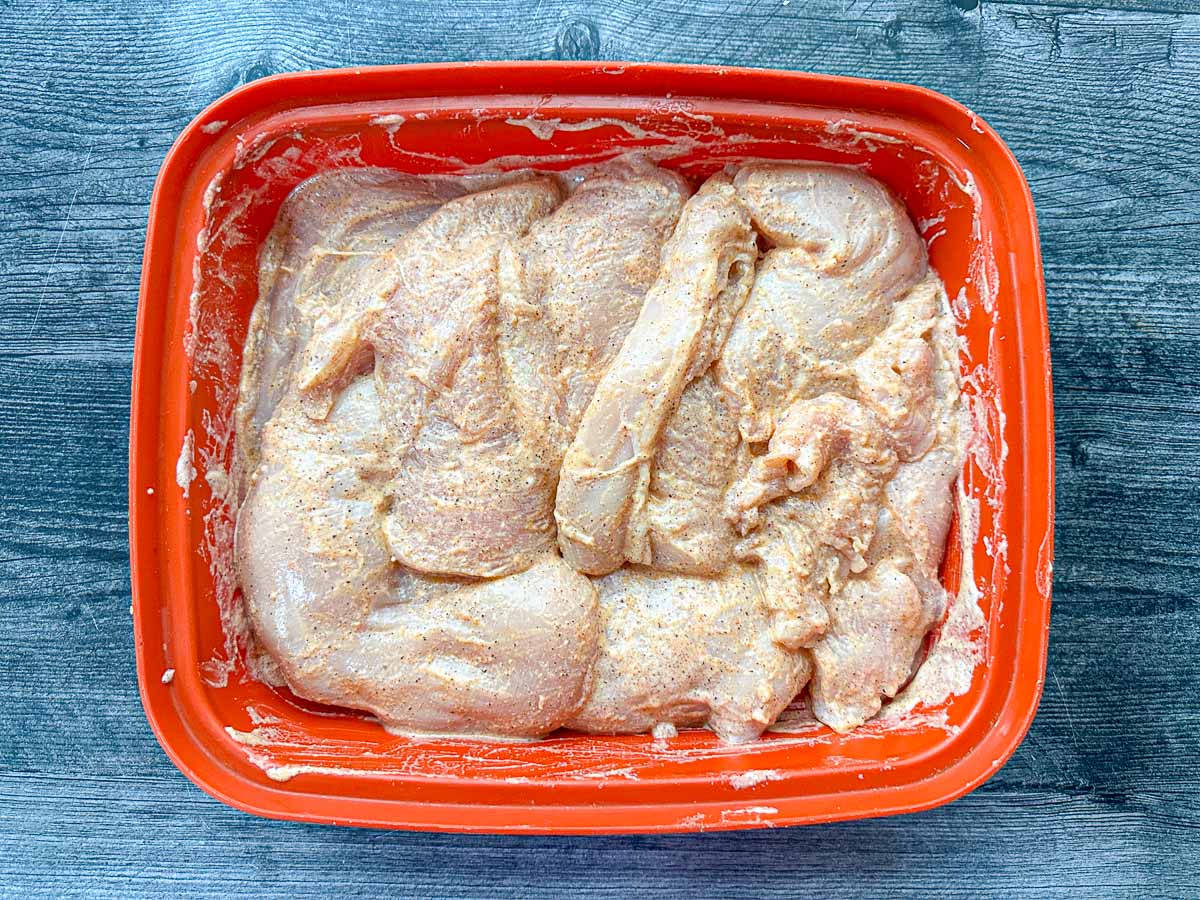 Marinating container with raw chicken in yogurt marinade.