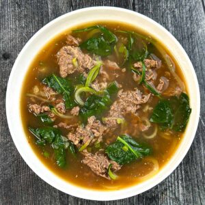 Aerial view of the a white bowl of the low carb Asian beef soup.