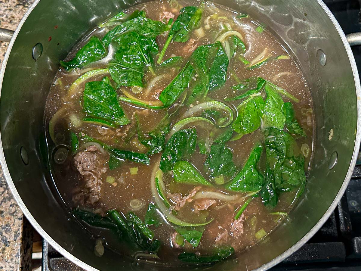 Soup pot with the spinach added after turning off the heat.