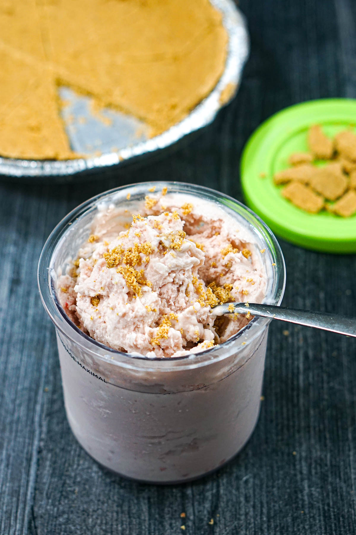 A pint container with the keto strawberry cheesecake ice cream and a store bought graham cracker crust in the background.