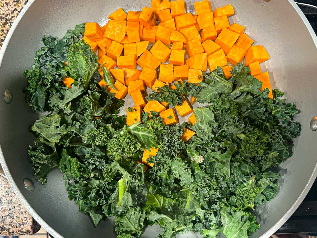 Large skillet with raw kale and sweet potato cubes.