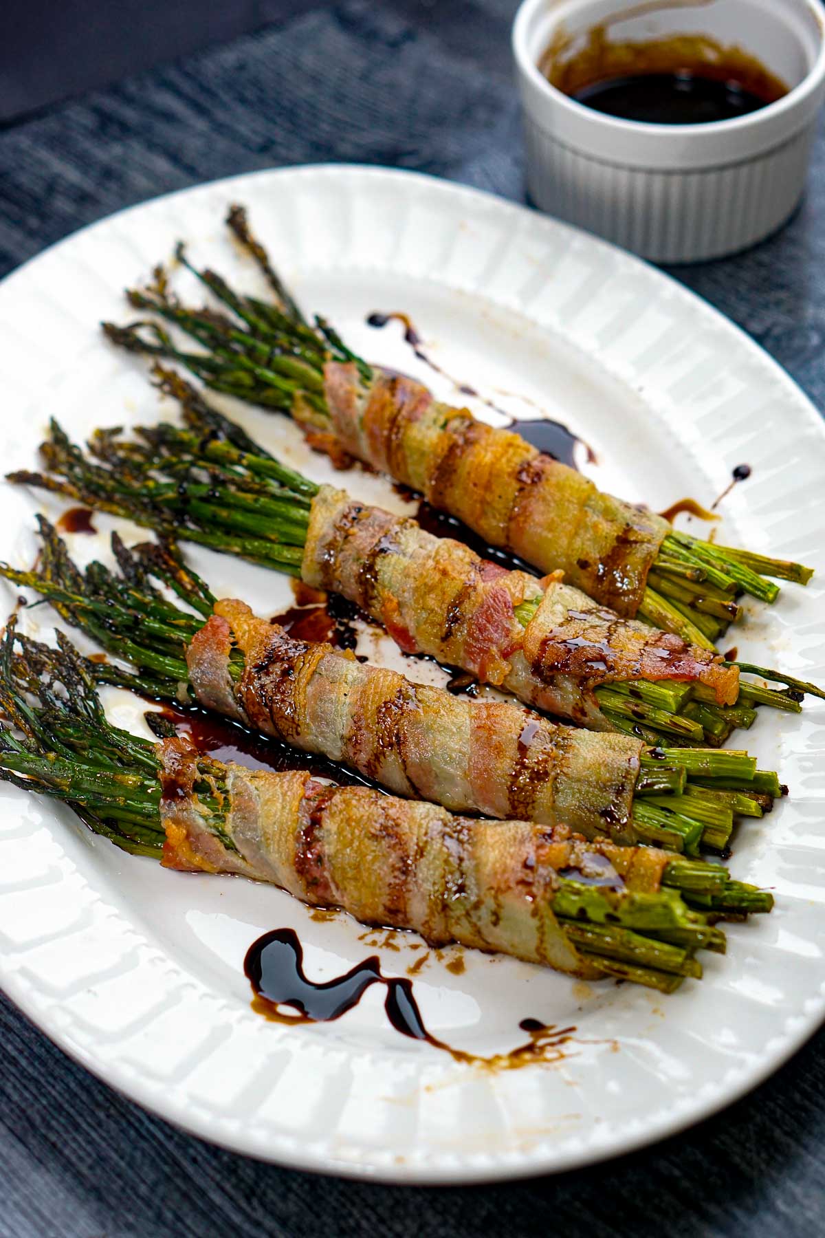 White platter with a 4 bacon wrapped asparagus bundles with balsamic glaze.