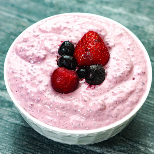 White bowl with the low carb yogurt chia seed pudding with a few berries on top.