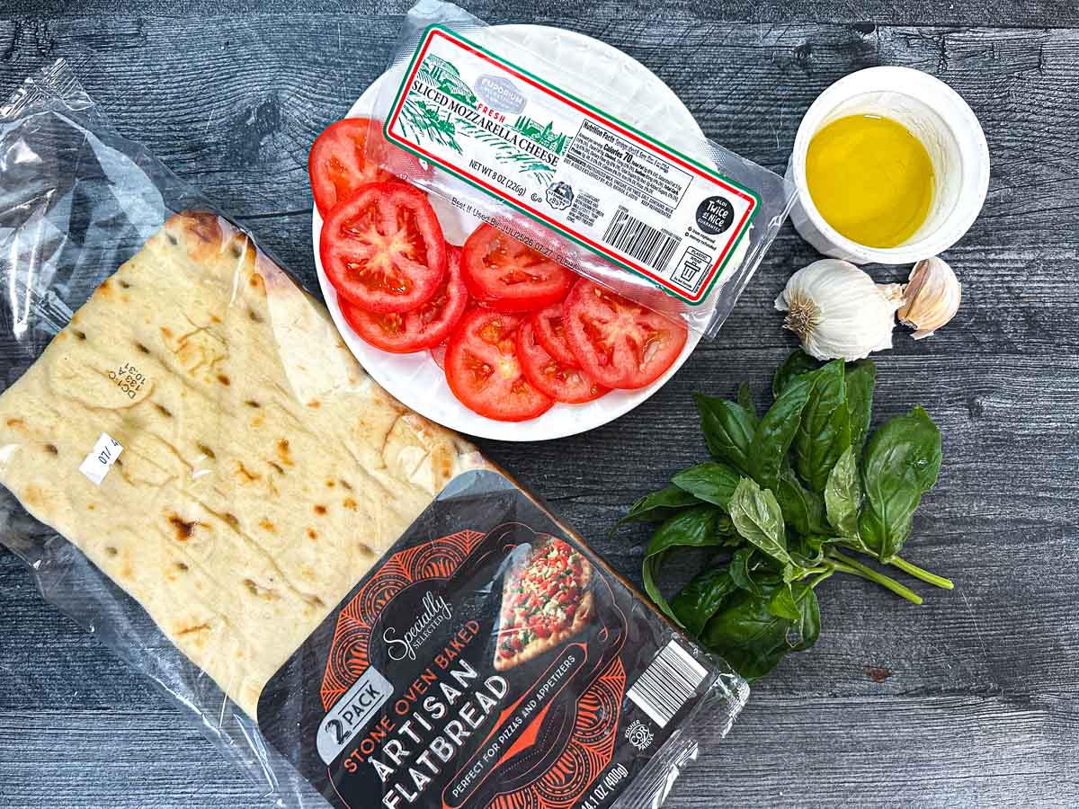 Recipe ingredients - a premade flatbread, sliced tomatoes, fresh mozzarella, olive oil, garlic.