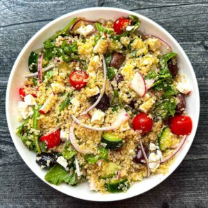 White bowl with arugula quinoa salad with Mediterranean flavors.