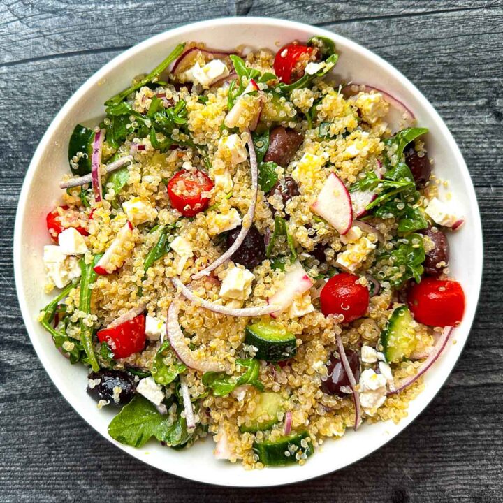 White bowl with arugula quinoa salad with Mediterranean flavors.
