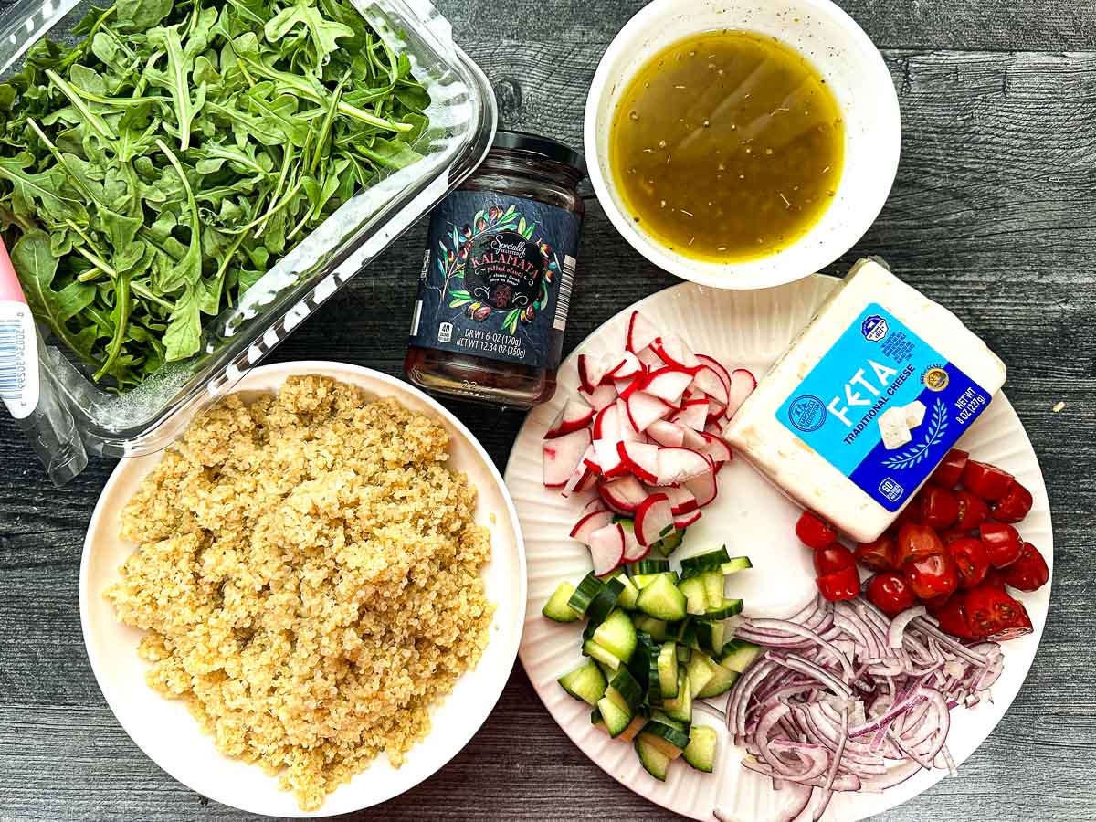 Recipe ingredients - arugula, quina, olives, dressing, feta, and chopped veggies.
