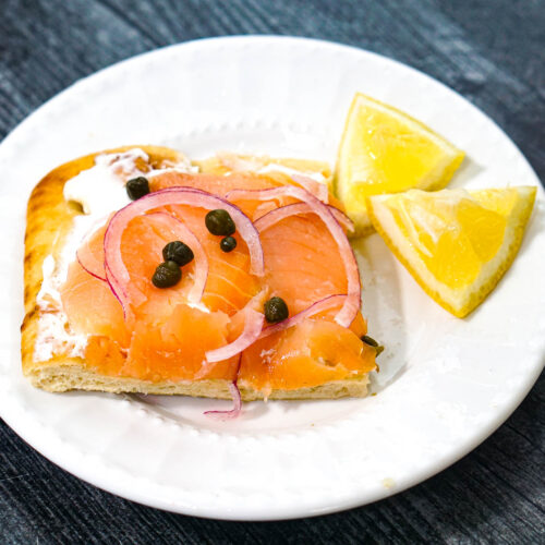 Closeup of a white plate with a slice of the smoked salmon flatbread and a couple lemon wedges.