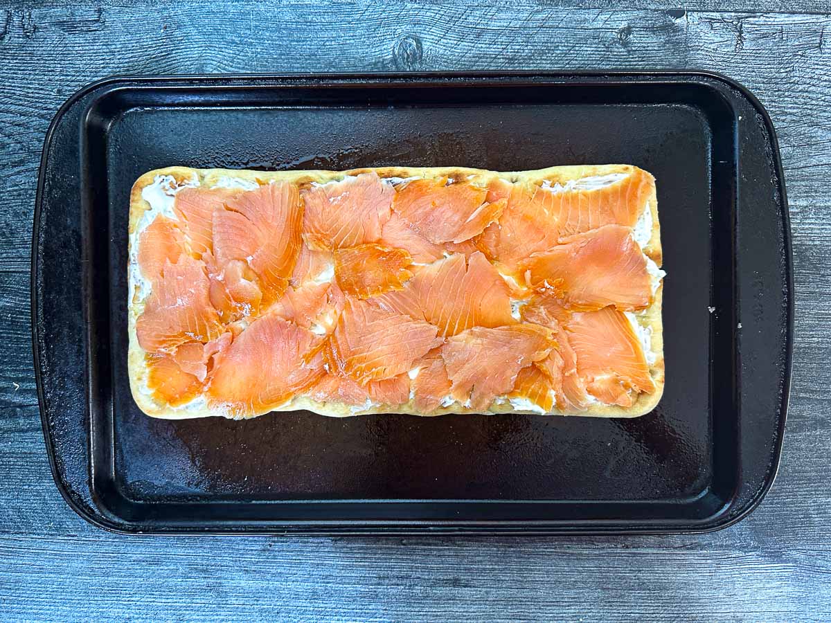 Baking sheet with a flatbread with cream cheese spread and topped with smoked salmon.