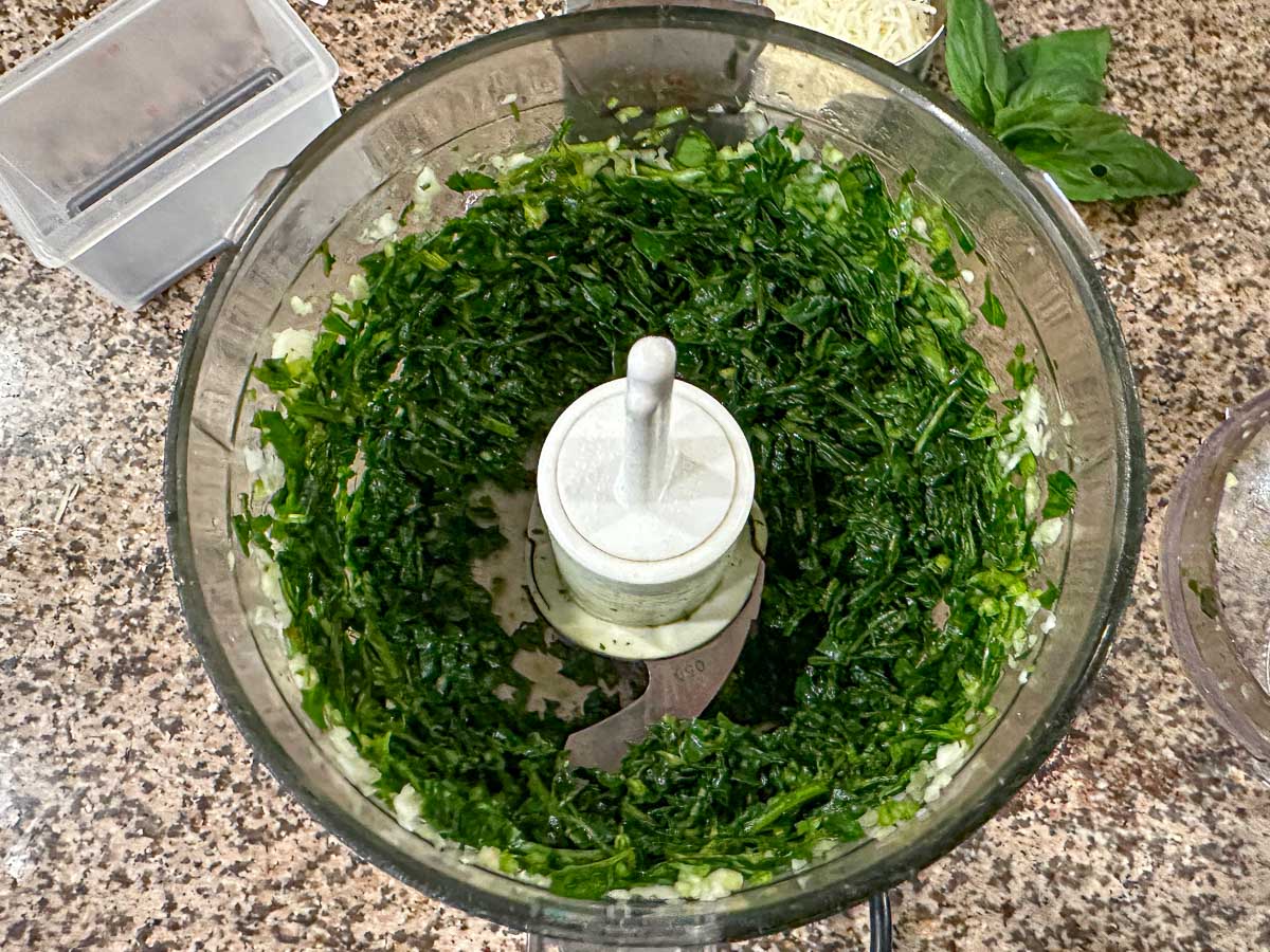 Food processor bowl with chopped basil and garlic.